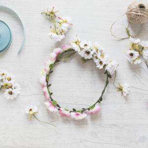 Couronne florale entourée de rubans, d'une bobine de ficelle et de ciseaux, posée sur un fond blanc texturé, prête à être finalisée.