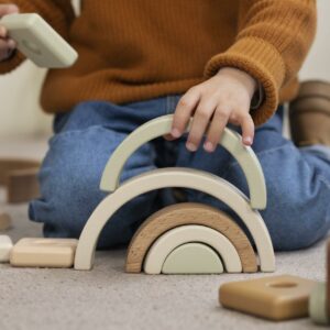 Garçon concentré en train de jouer avec des jouets écologiques en bois à l'intérieur, dans un espace inspiré par la pédagogie Montessori.