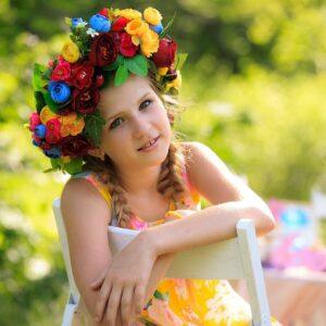 Petite fille souriante portant une couronne florale colorée sur la tête, prête à célébrer le carnaval.