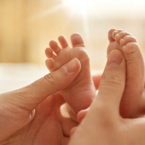 Pieds de bébé massés délicatement, mettant en valeur un moment de détente et de connexion entre le parent et l'enfant.