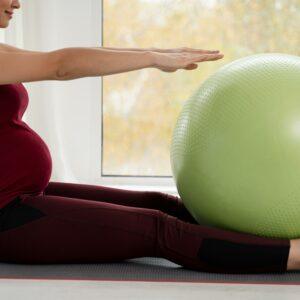 Femme enceinte en train de faire des exercices doux avec un ballon de fitness vert pendant une séance de yoga prénatal.