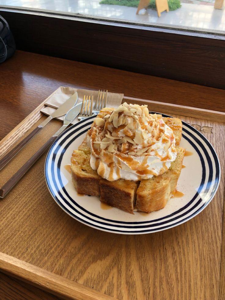 Honeybread (pain toaster et miel) poser servie sur un plateau dans un café avec des couverts et de la chantilly sur le dessus.