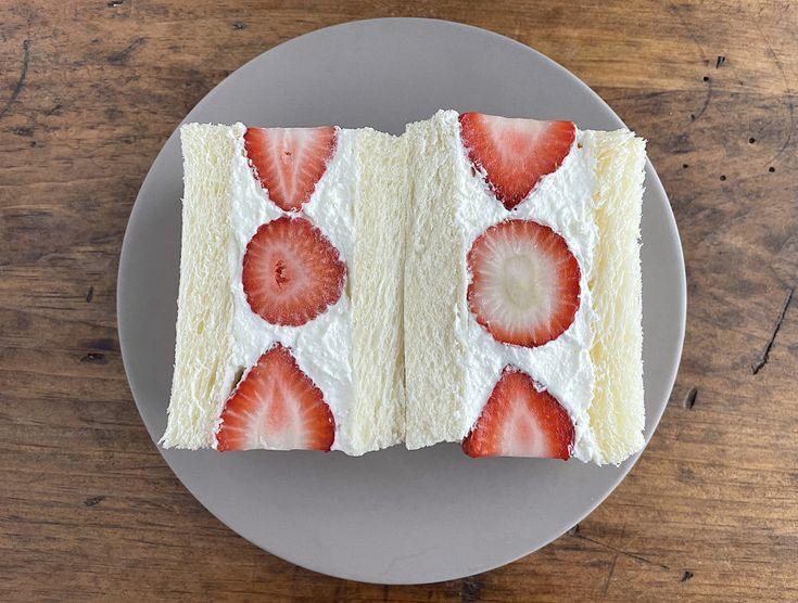 Sandwich coupé en deux avec de la crème fouetté et des fraises coupées à l'intérieur, posé dans une assiettes sur une table en bois