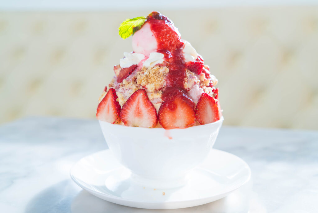 Bingsu à la fraise avec des morceaux, de la glace, du coulis et du crumble présenter dans un petit bol sur une assiette