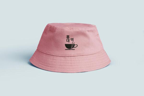 Bob de couleur rose sur fond gris, élément graphique du logo en noir qui est au milieu du bob