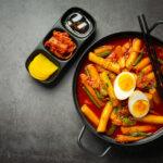 Plat coréen, le tteokbokki et des accompagnements, le tout sur un fond gris.