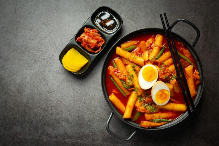 Plat coréen, le tteokbokki et des accompagnements, le tout sur un fond gris.