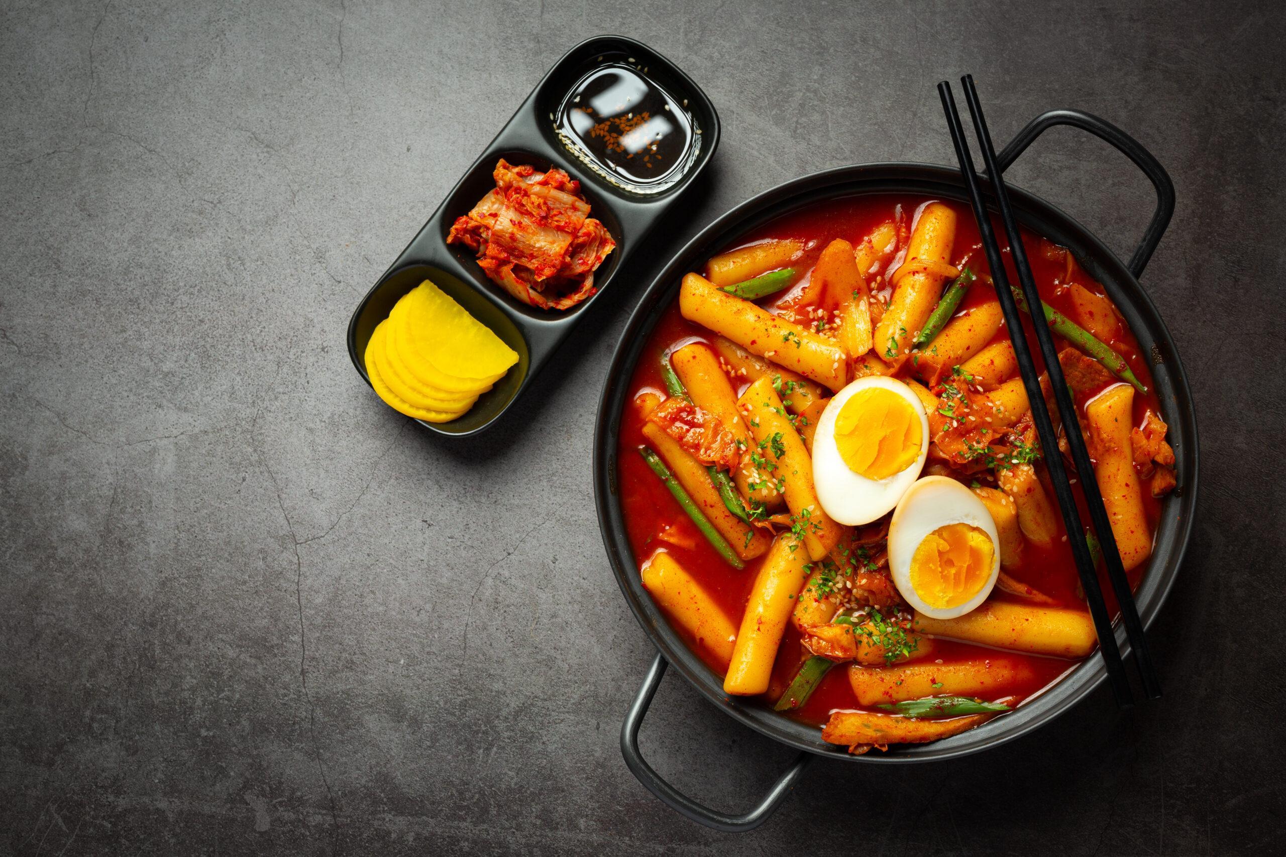 Plat coréen, le tteokbokki et des accompagnements, le tout sur un fond gris.