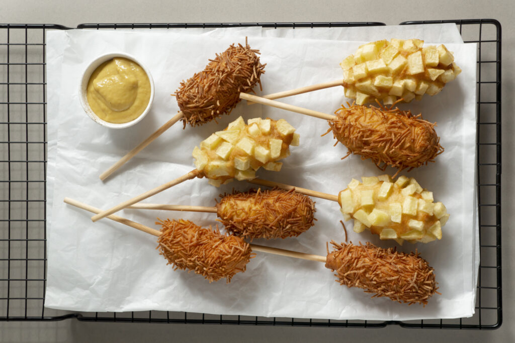 Corn dog déposés sur une plaque de cuisson avec du papier et un petit bol de sauce