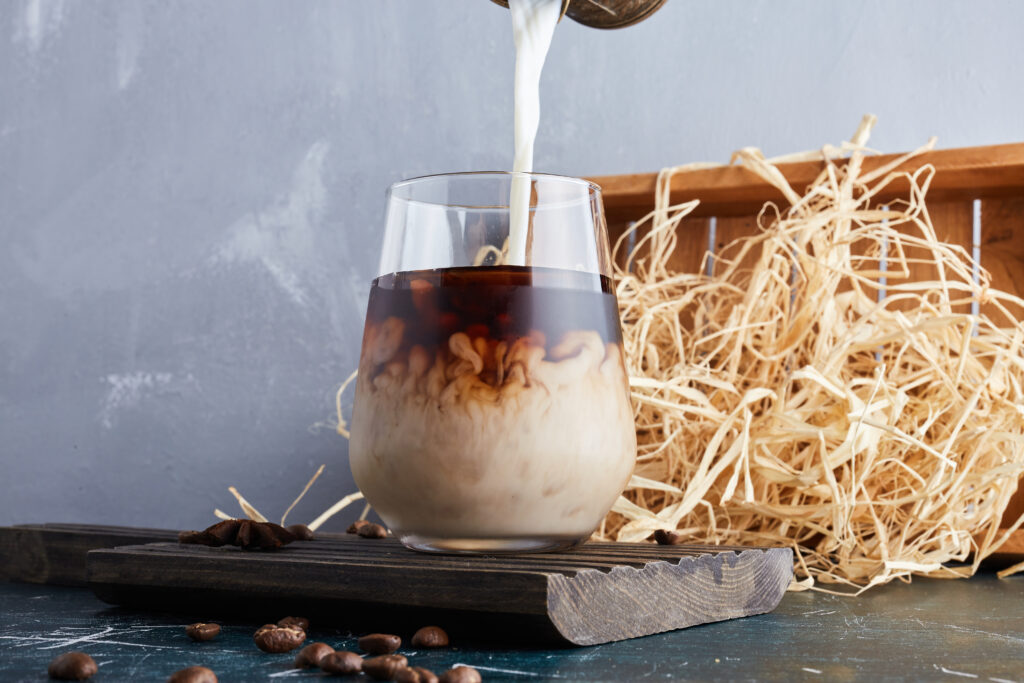 Lait qui est versé dans un verre rempli de café pour en faire un café latte