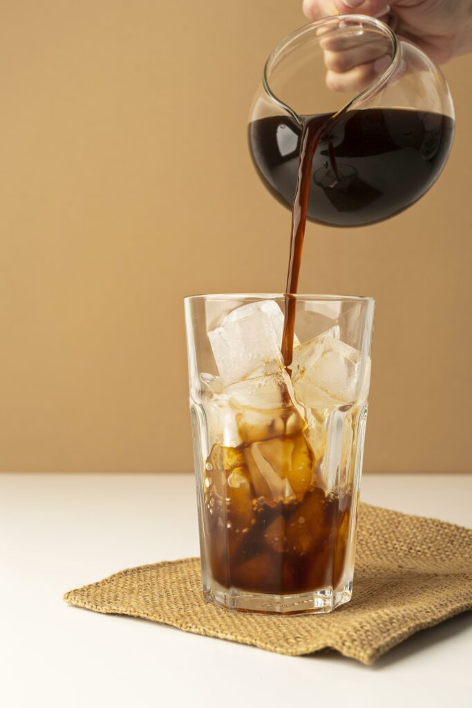 Café qui est versé dans un verre rempli de glaçons pour faire un ice americano.