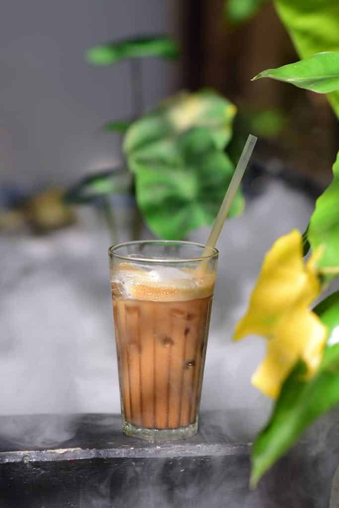 A chilled glass of iced coffee surrounded by lush greenery, evoking a refreshing tropical vibe.