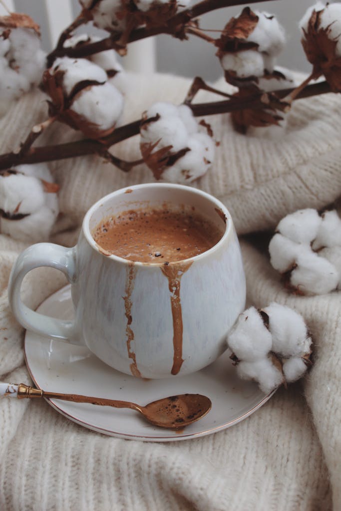 A steaming cup of hot chocolate surrounded by cotton flowers on a soft knit background.