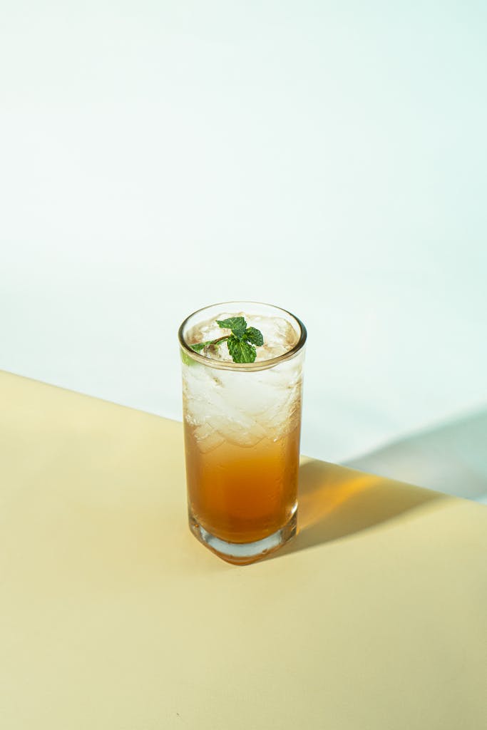 A tall glass of iced tea with mint leaves on a pastel background.
