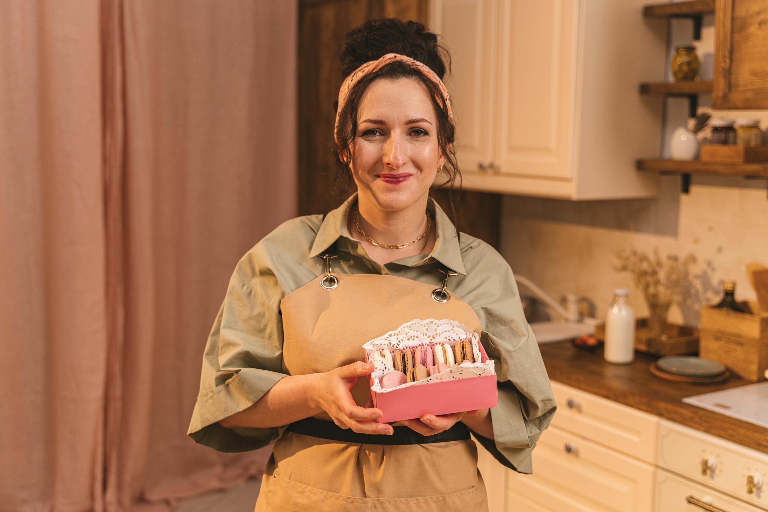 Femme souriante avec un tablier de cuisine tenant un paquet de macarons dans les mains