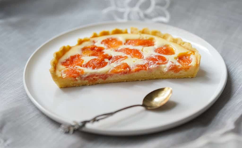 Close-up of a freshly baked apricot tart slice served on a white plate.