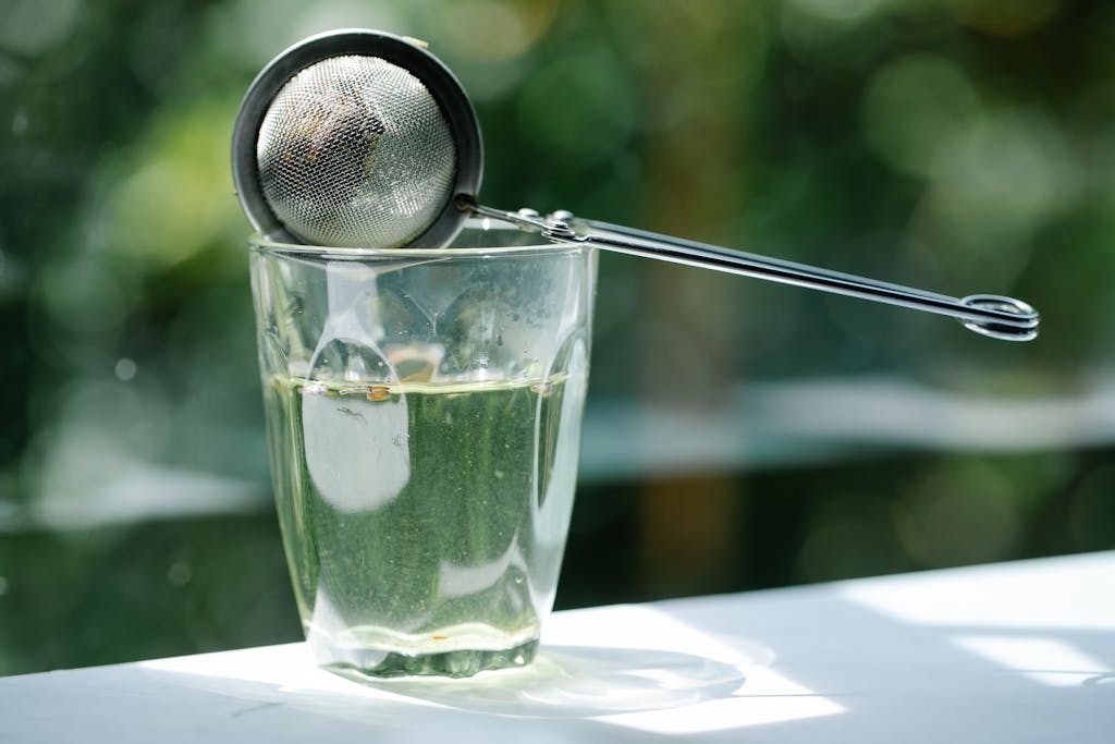 Close-up of glass with tea infuser in sunlight, highlighting serenity and refreshment.