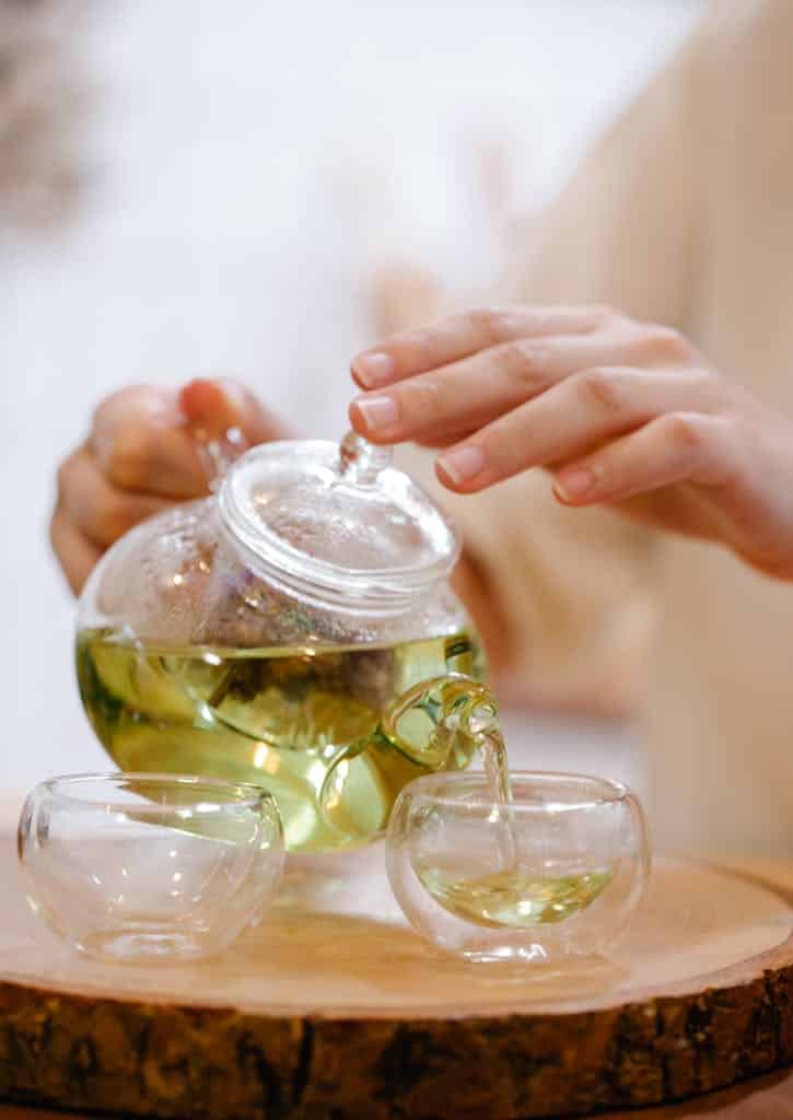 Close-up of pouring green tea from a teapot into glass cups, creating a serene moment.