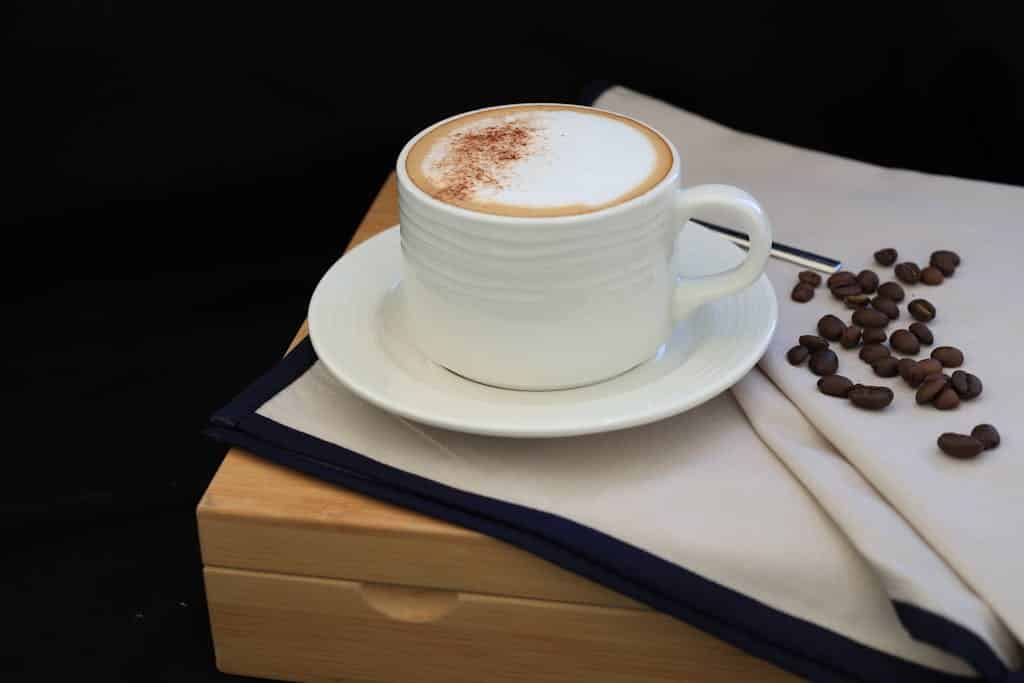 Elegant cappuccino setup with coffee beans on a wooden tray, showcasing a peaceful coffee moment.