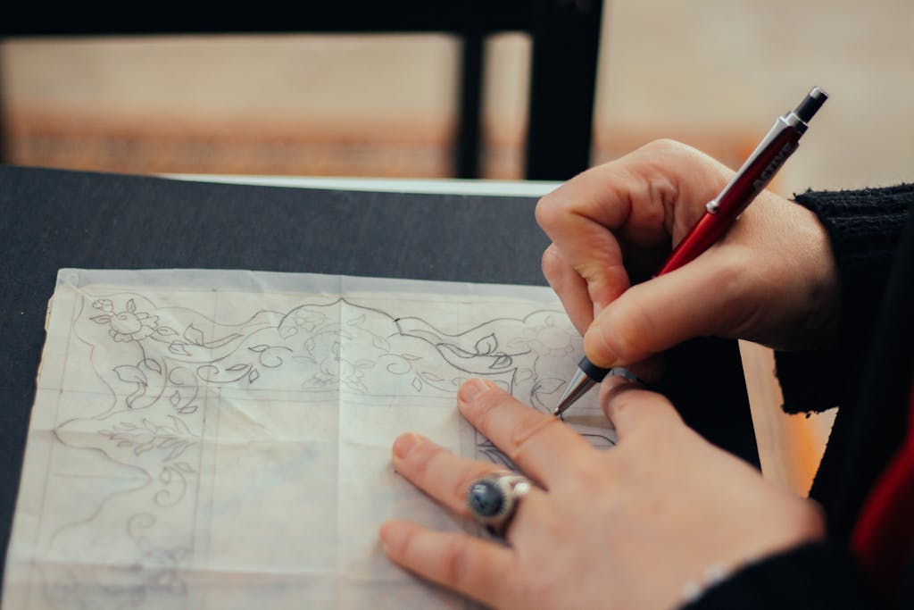Hands sketching floral designs on tracing paper with a pencil, showcasing creativity and artistry.