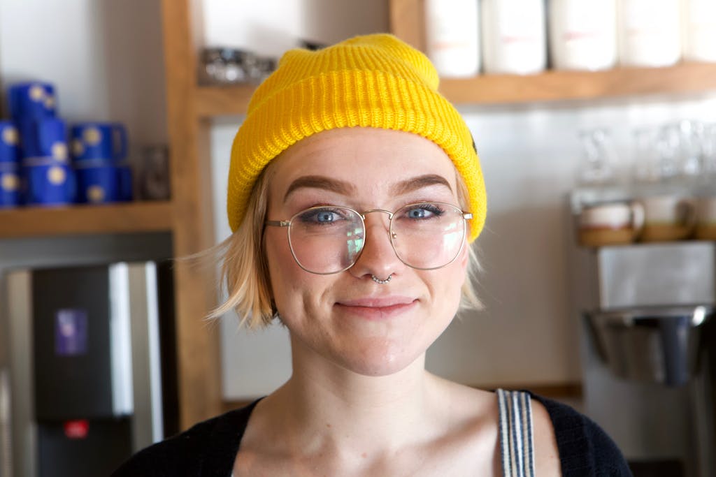 Portrait of a stylish young woman with glasses and beanie smiling indoors. Perfect for lifestyle and fashion concepts.