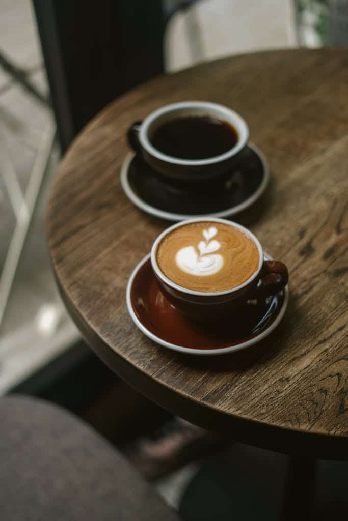 Warm café setting with a cappuccino and espresso on a wooden table, perfect for relaxing moments.