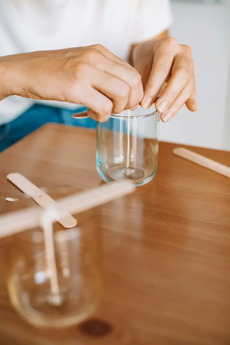 Mains collant une mèche de bougie dans un conteneur en verre