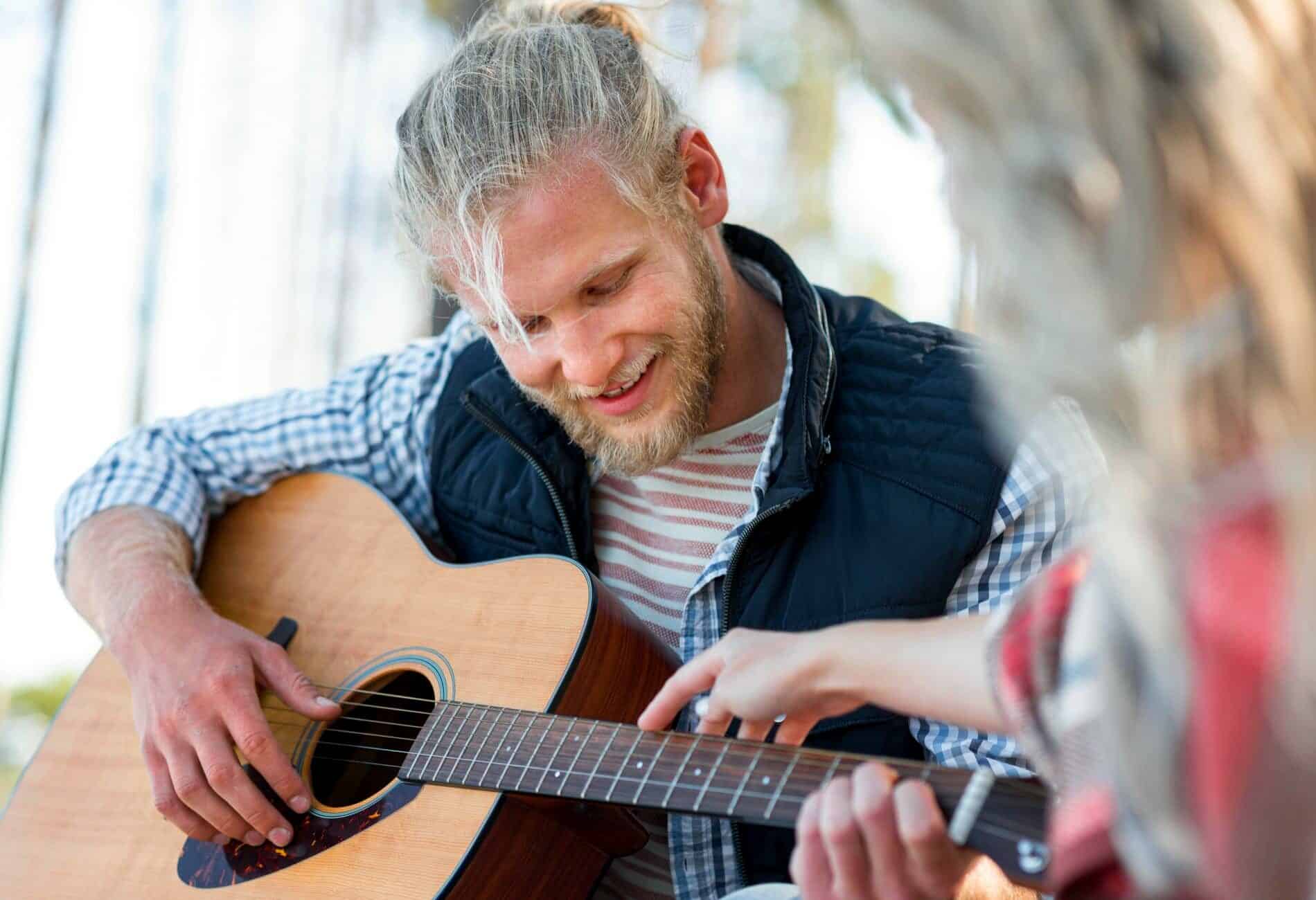 homme tenant une guitare se faisant aider par une autre personne